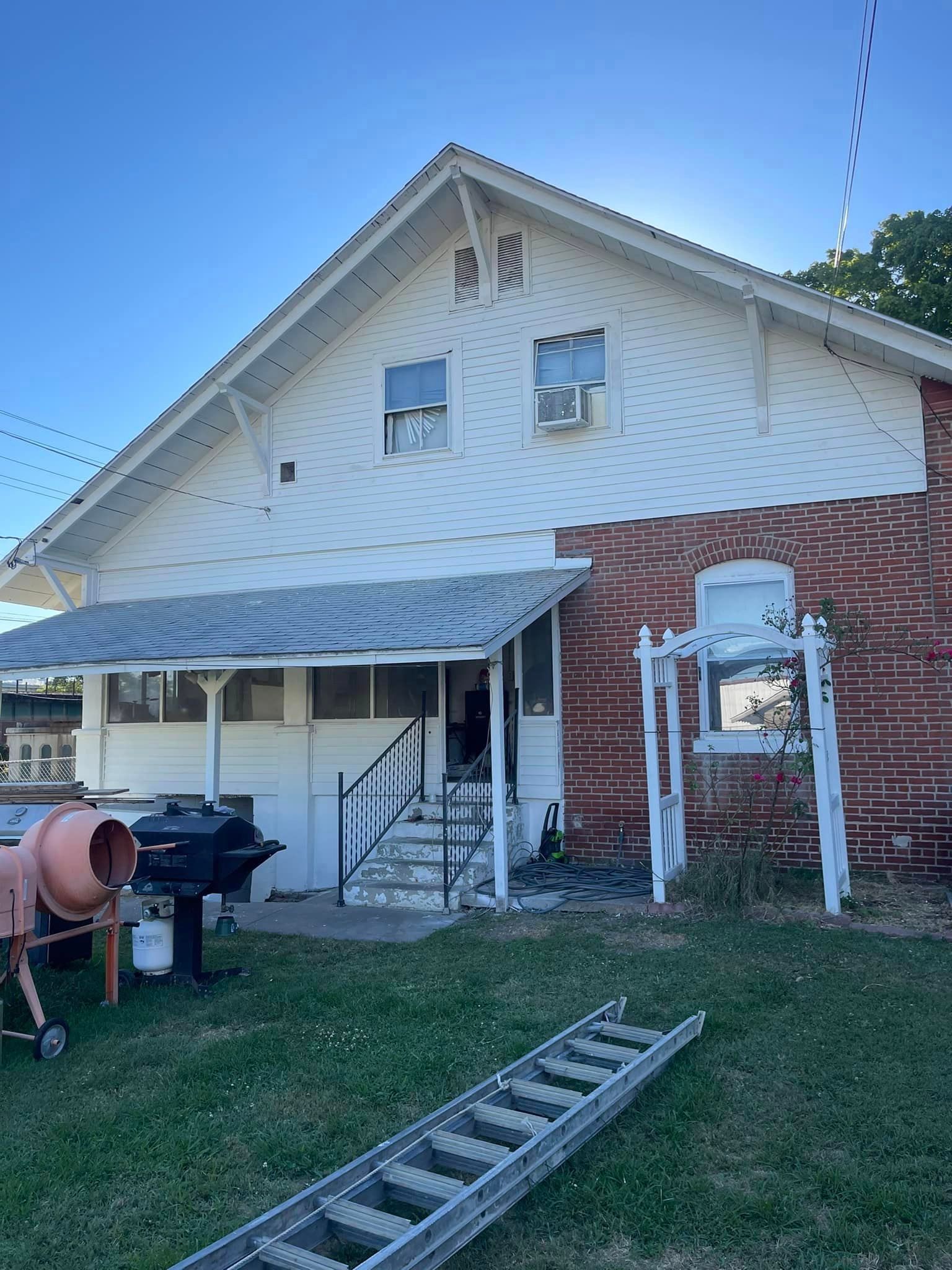 A white house with a brick wall and a ladder in front of it.