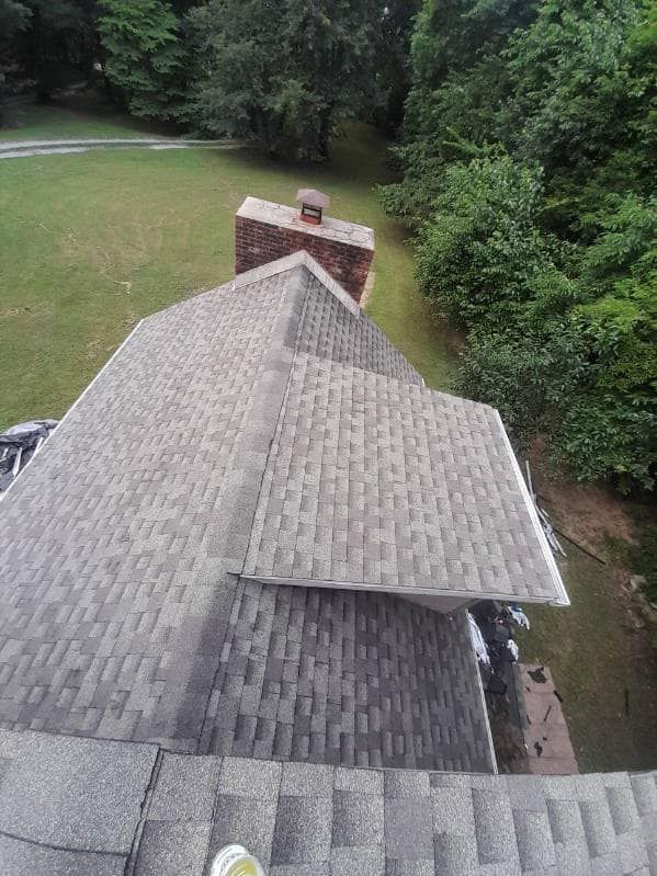 An aerial view of a roof with a chimney and trees in the background.