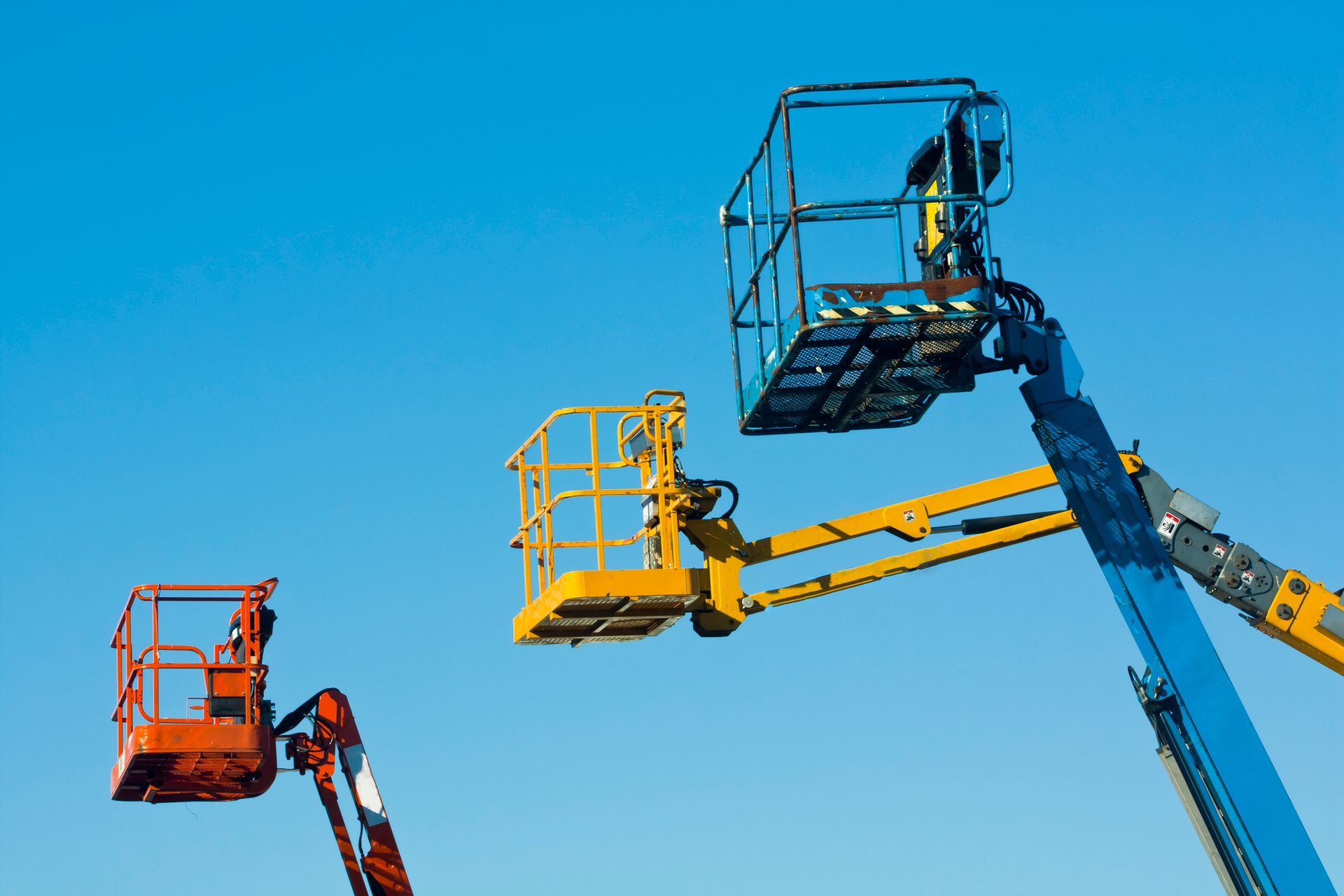 Row of three tall, multi-coloured boom lifts.