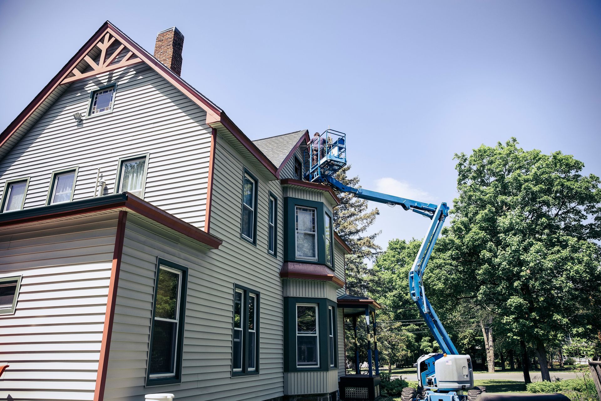 Man standing on boom lift repairing home exterior.