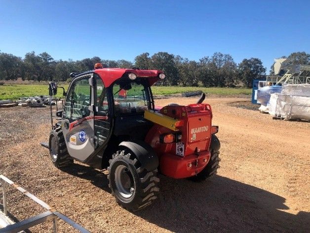 A red and black tractor parked on a dirt surface.