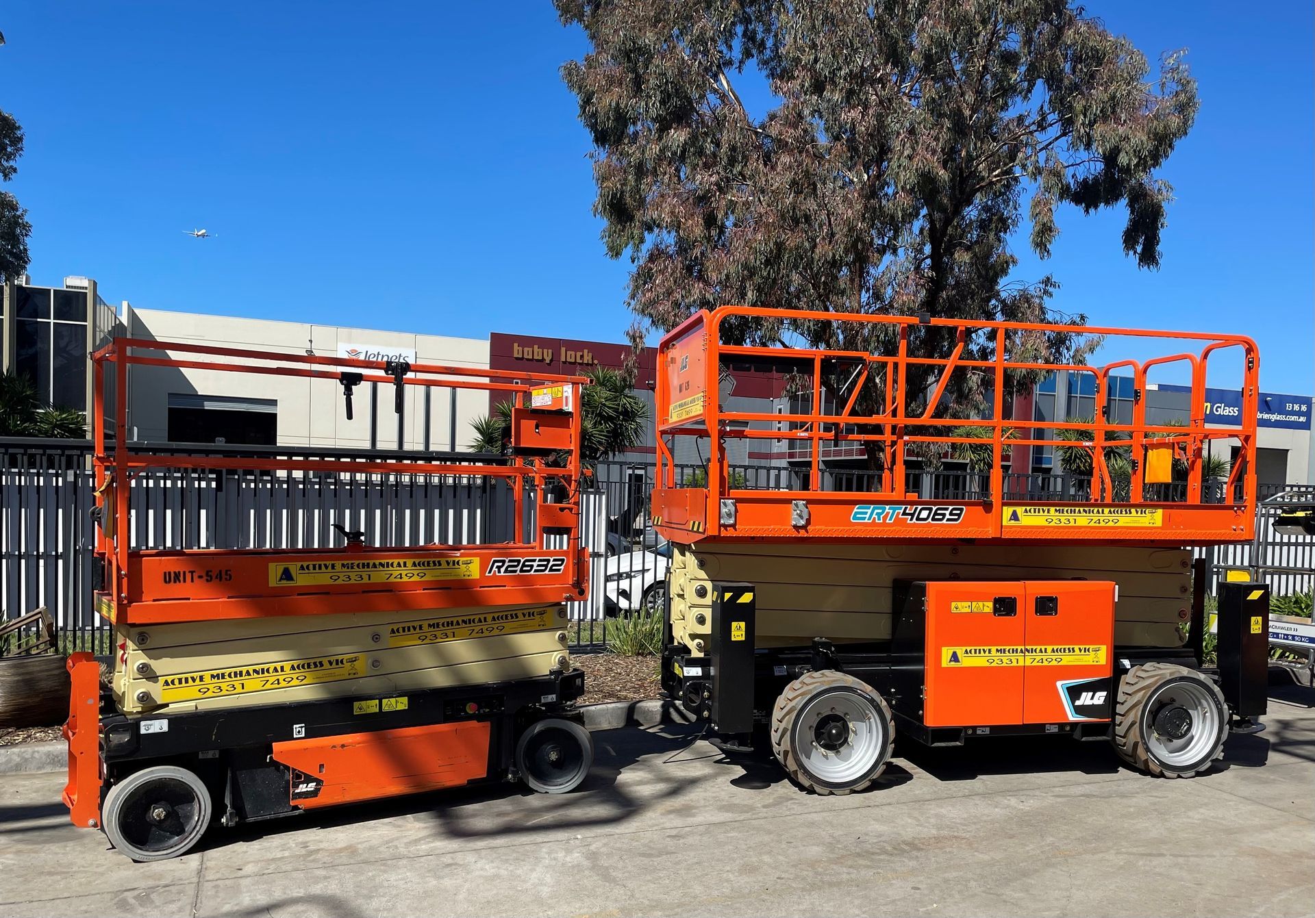 Two orange scissor lifts are parked next to each other