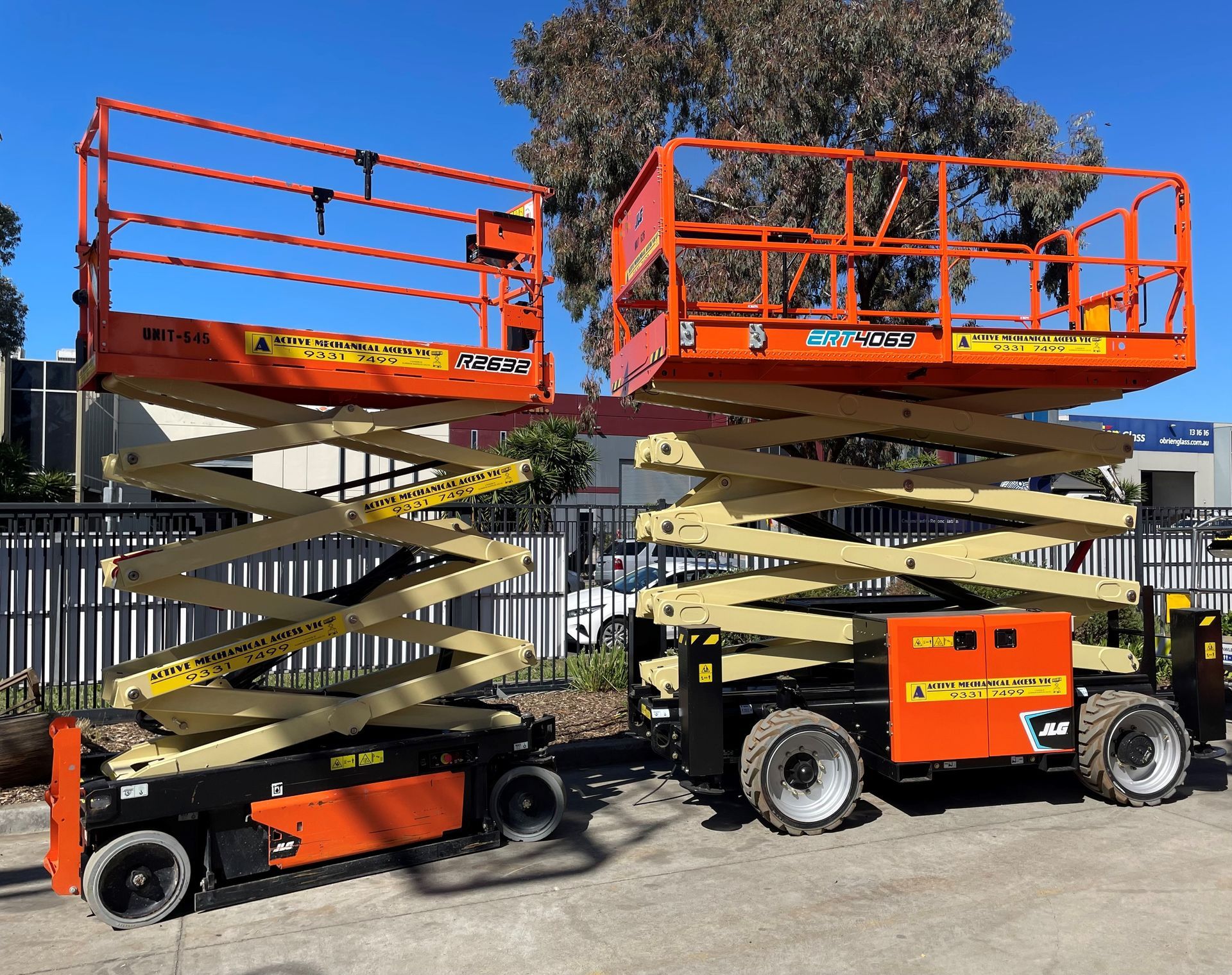 A red and black crane is sitting in a parking lot with trees in the background