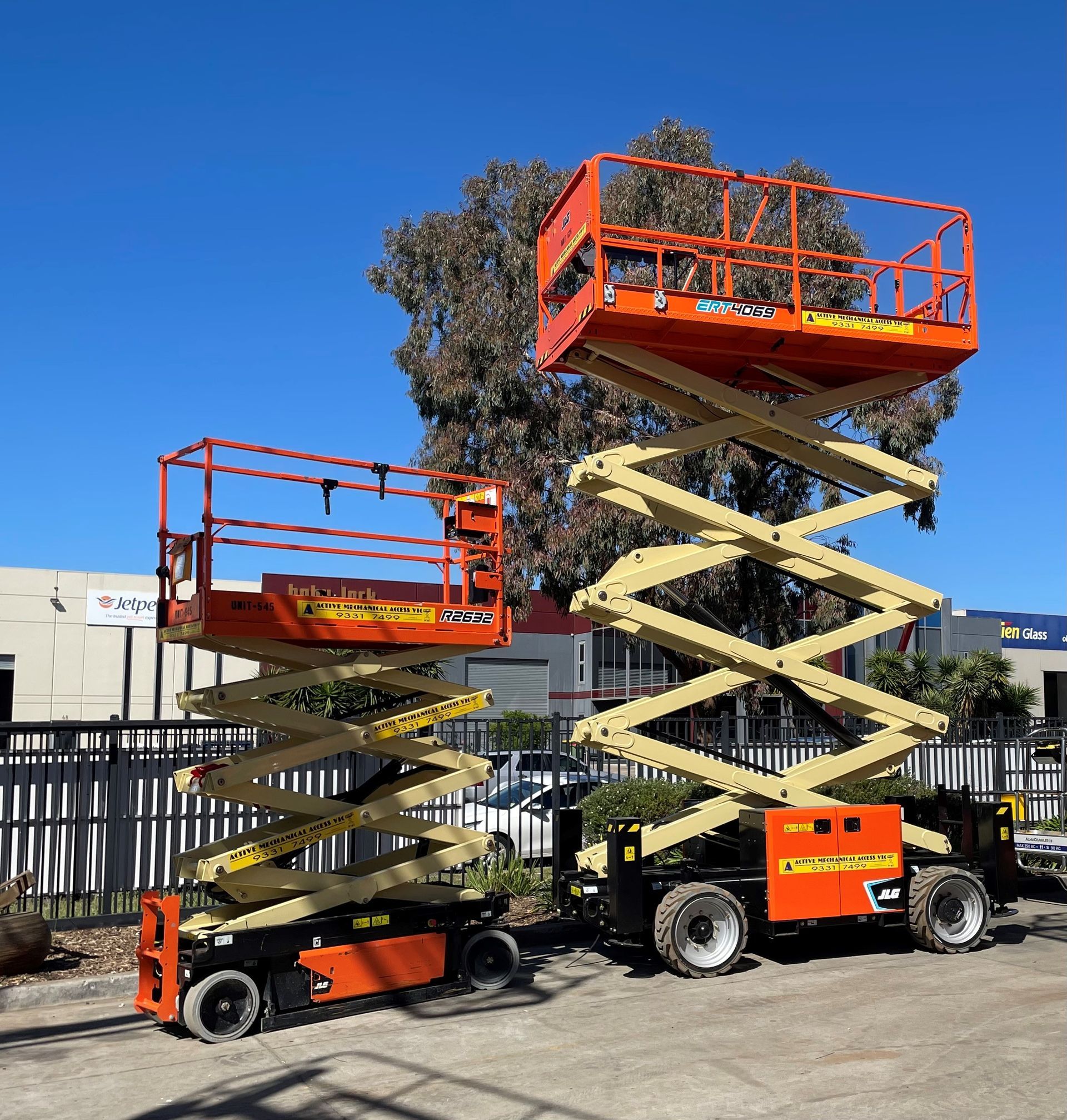 Two orange scissor lifts are parked next to each other