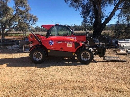 A red tractor equipped with a large forklift attachment, positioned in a farm setting