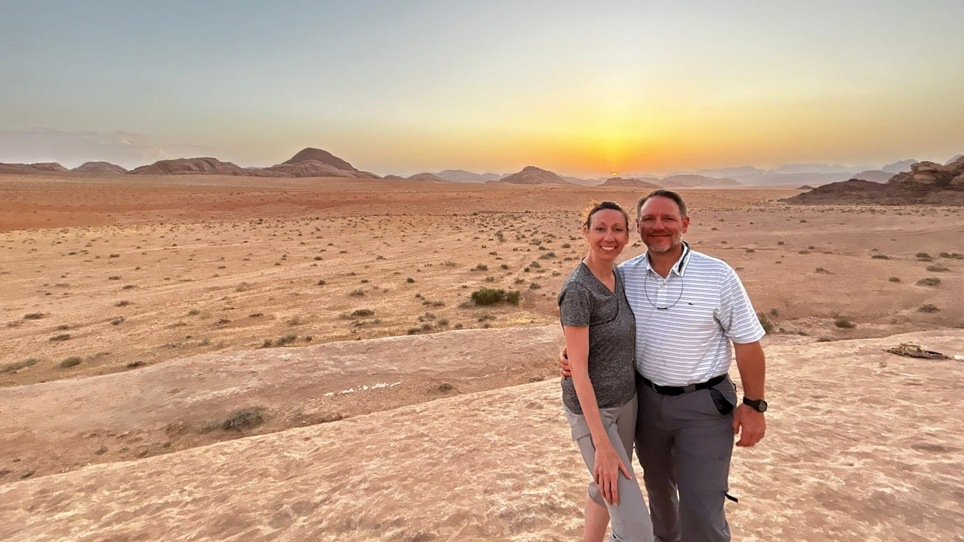 A man and a woman are posing for a picture at Wadi Rum at sunset.