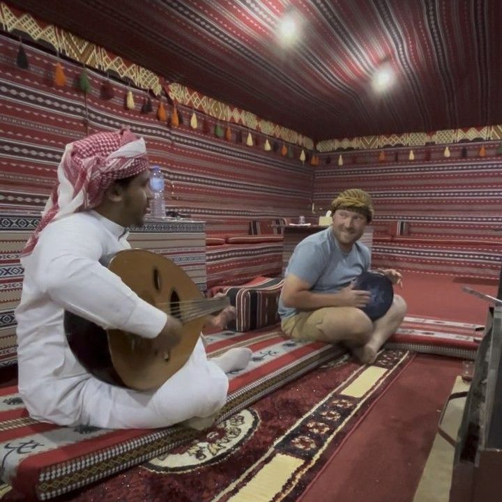 A bedouin is playing a guitar while another man plays a drum 