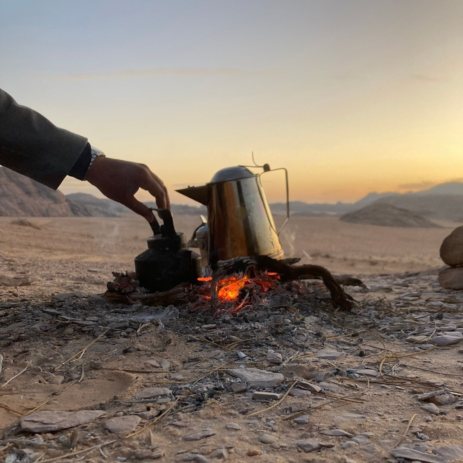 A person is pouring tea into a kettle over a fire in the Wadi Rum