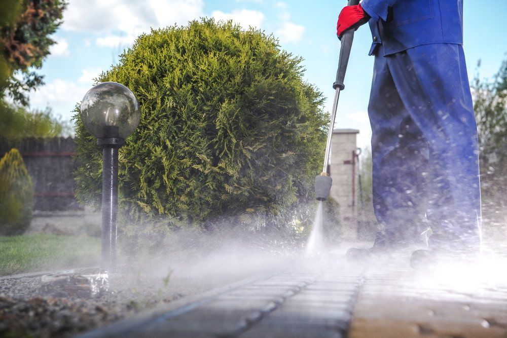 A Man Is Using A High Pressure Washer To Clean A Brick Walkway — Darren's Mowing In Moss Vale, NSW