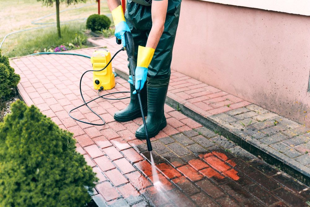 A Man Is Cleaning A Brick Sidewalk With A High Pressure Washer — Darren's Mowing In Miranda, NSW