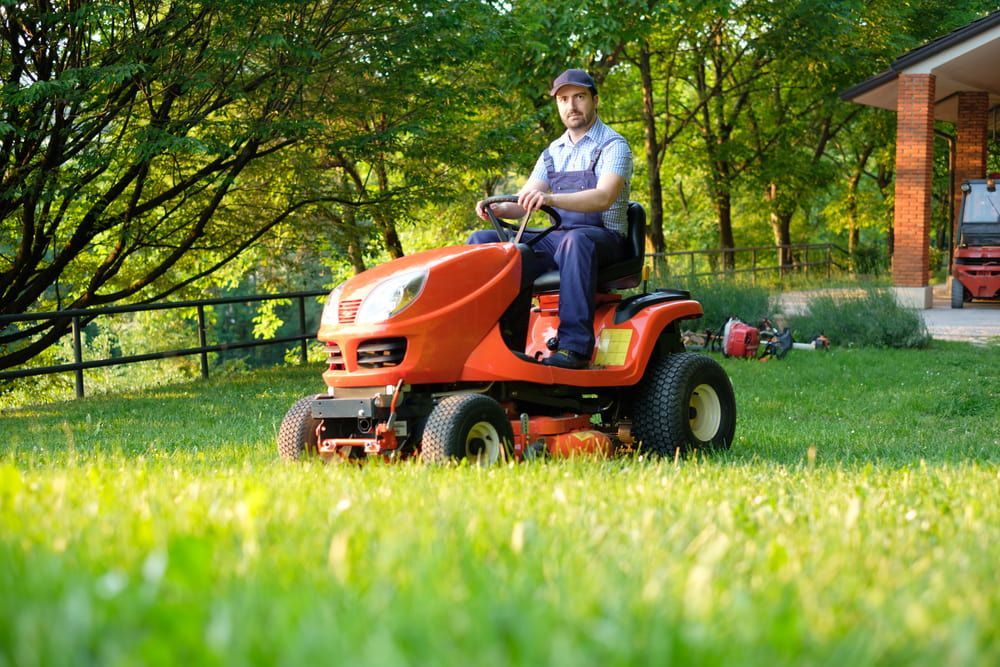 A Man Is Riding A Lawn Mower On A Lush Green Lawn — Darren's Mowing In Mittagong, NSW