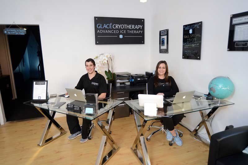 a man and a woman are sitting at a desk with laptops at one of the first cryotherapy locations in America