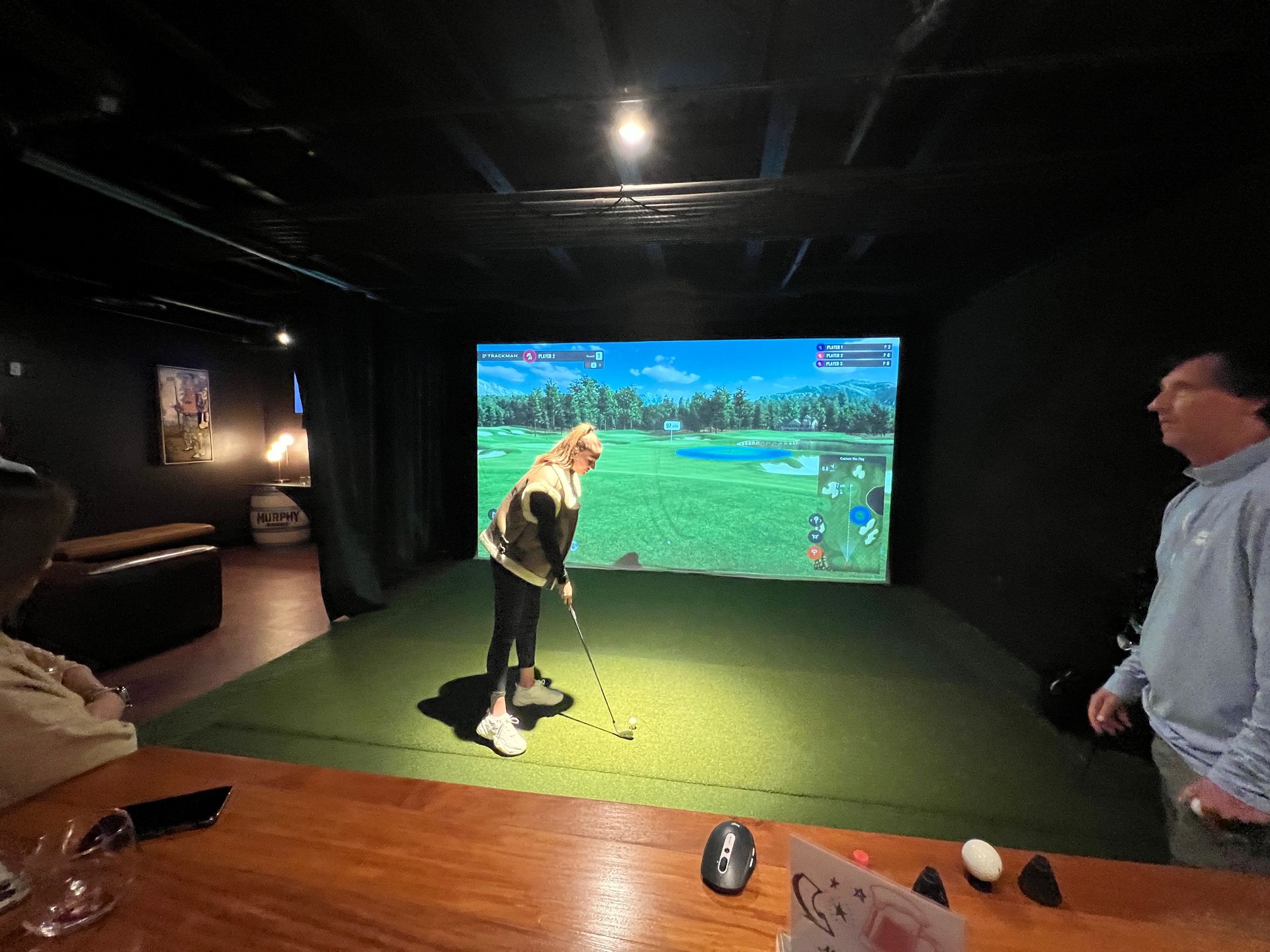 a woman is playing golf in a simulator while a man watches at an event called the cryo ranch 