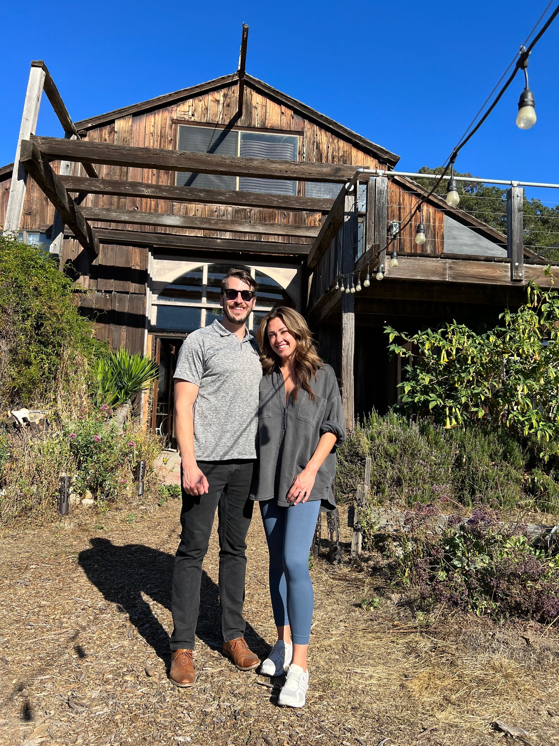 Skyler Scarlett and Lindsay Kirby are standing in front of a wooden house at a the cryo ranch.
