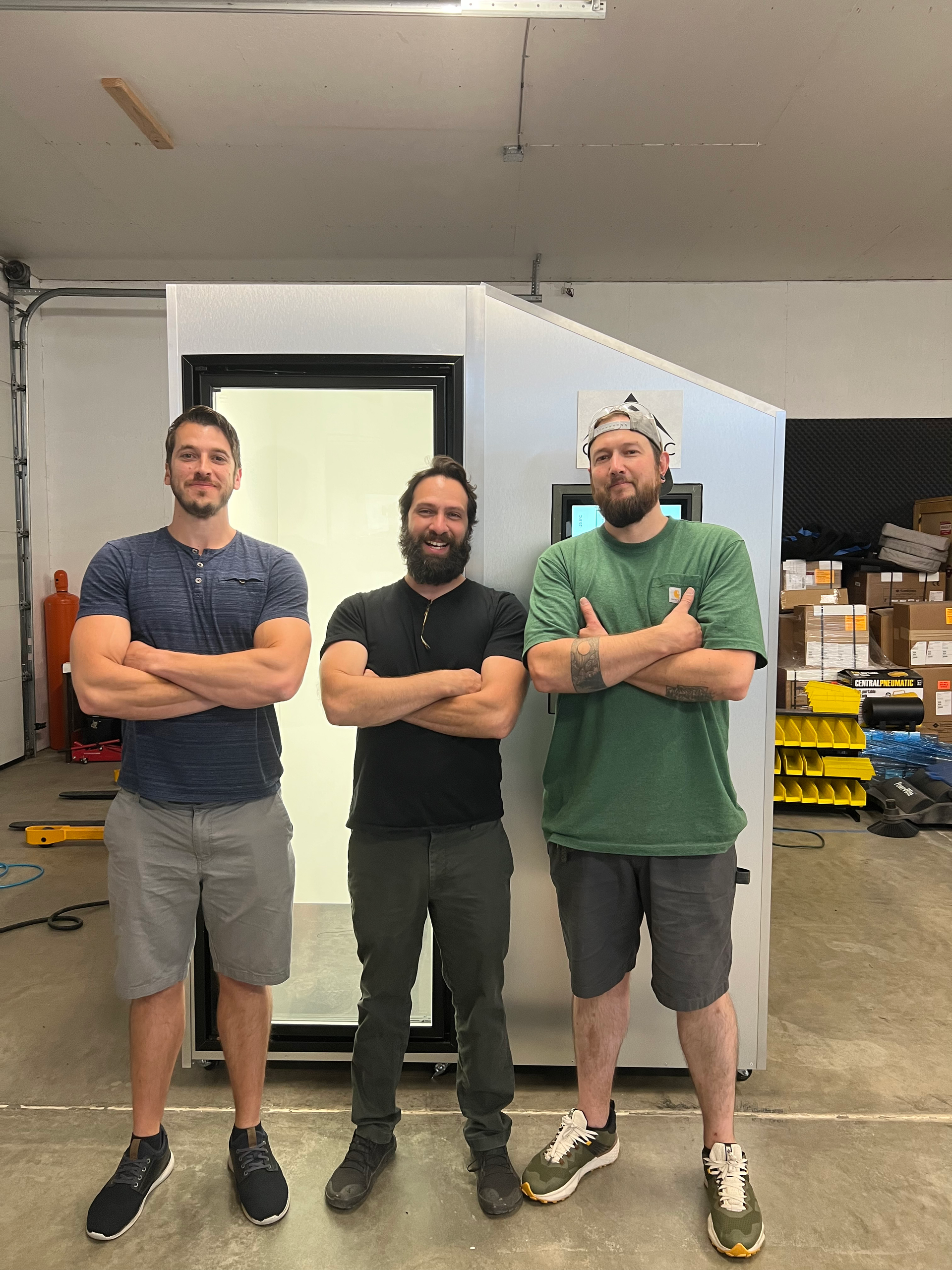 three men are standing in front of a cryo machine with their arms crossed .