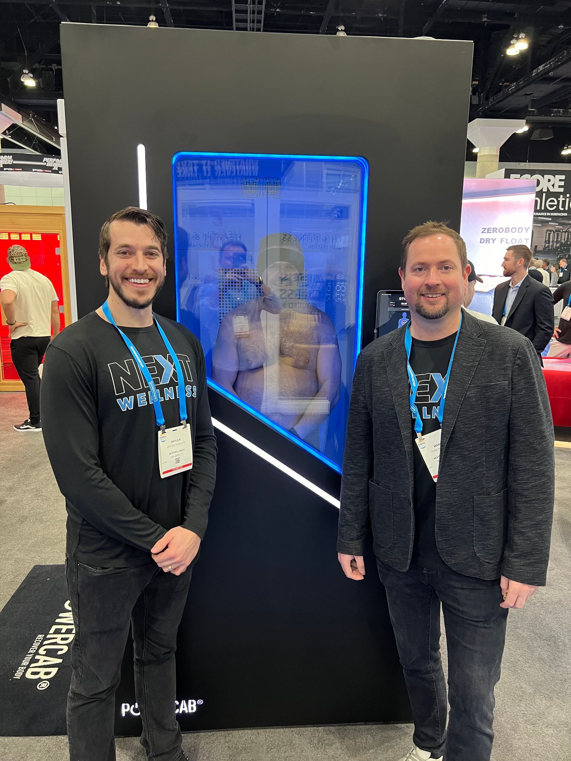 Two men are standing next to each other in front of a large screen.