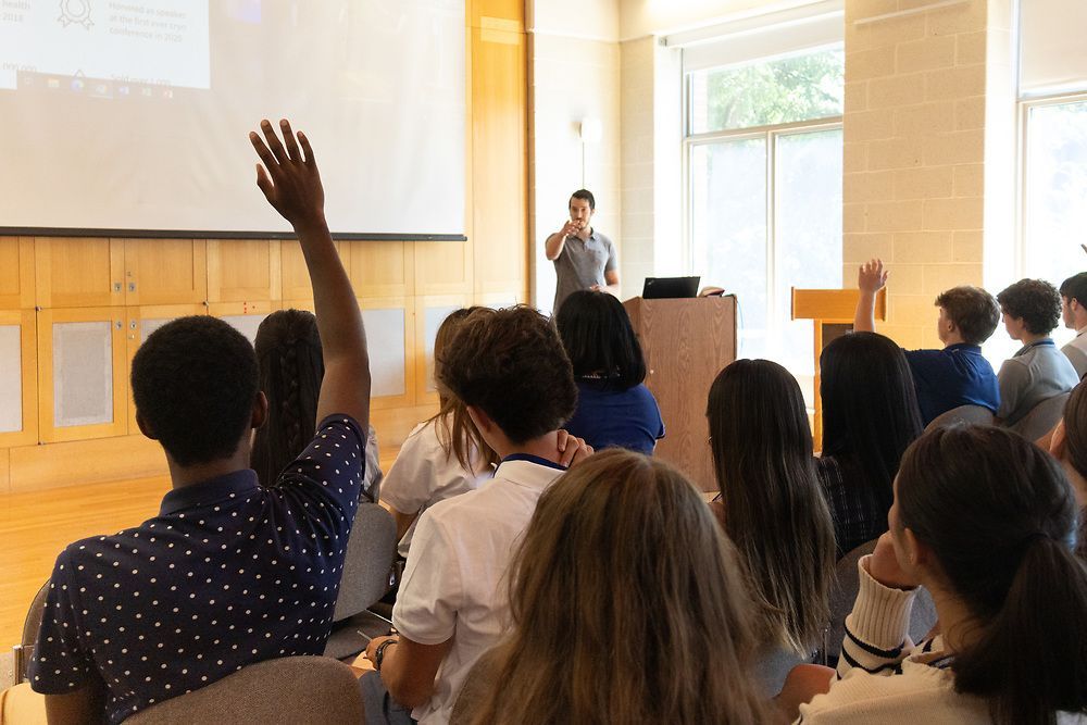 A group of people are sitting in a lecture hall raising their hands to answer a question.