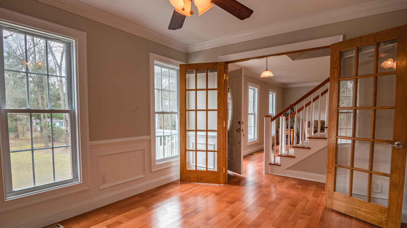 Room with wood floors, windows, French doors, and a staircase. Light brown walls and trim.