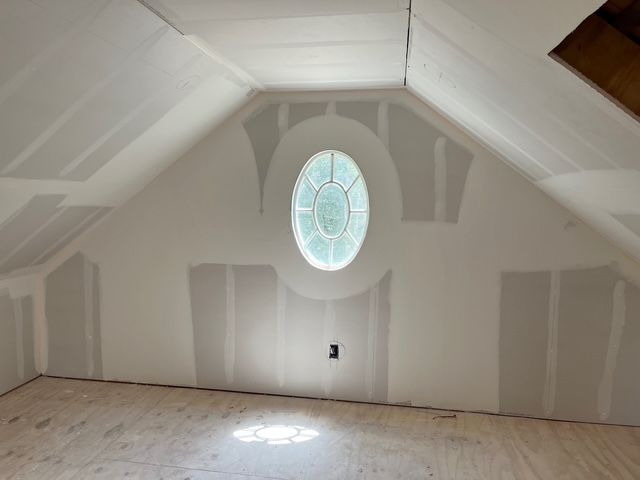 Interior attic room with drywall, oval window, and wood floor.
