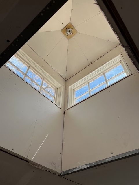 Interior view of a triangular skylight with two windows. Walls are white and a light fixture is visible at the apex.