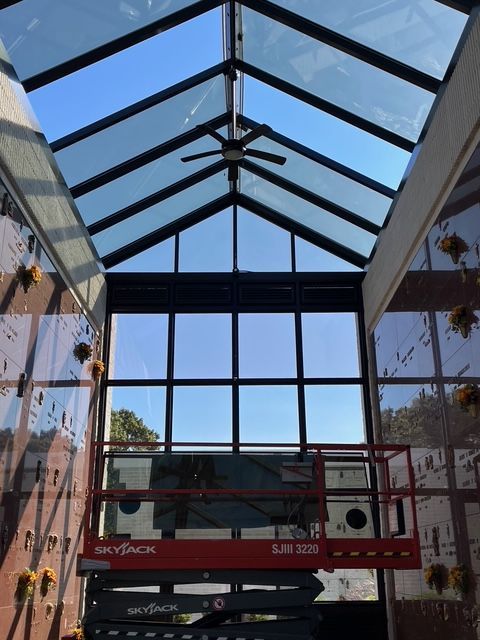 Interior of mausoleum with glass ceiling and large window, sunlight, red scissor lift.