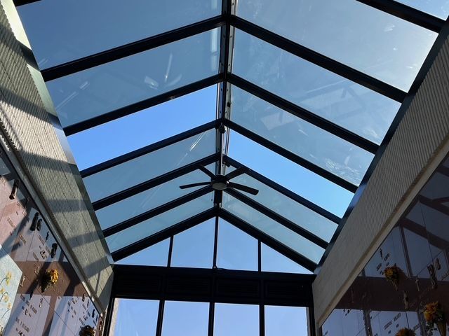Glass skylight with black beams, ceiling fan, and blue sky.