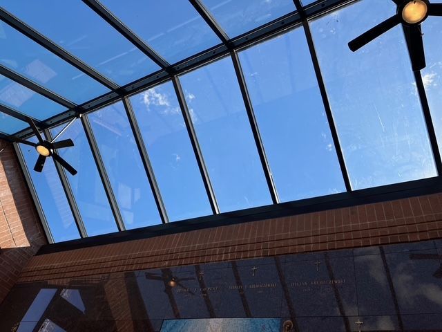 Skylight in a brick-walled room looking up at blue sky and clouds; ceiling fans visible.