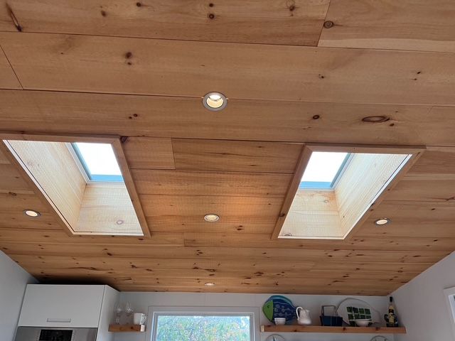 Wooden ceiling with two skylights and recessed lighting in a kitchen.