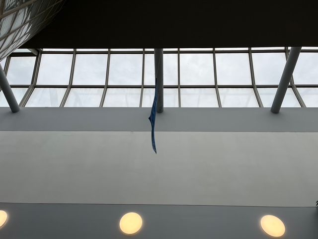 Blue object suspended from the ceiling in a brightly lit, modern building with skylights.