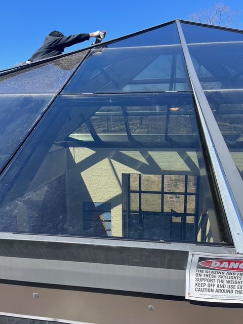 Person cleaning a glass pyramid roof.  A 