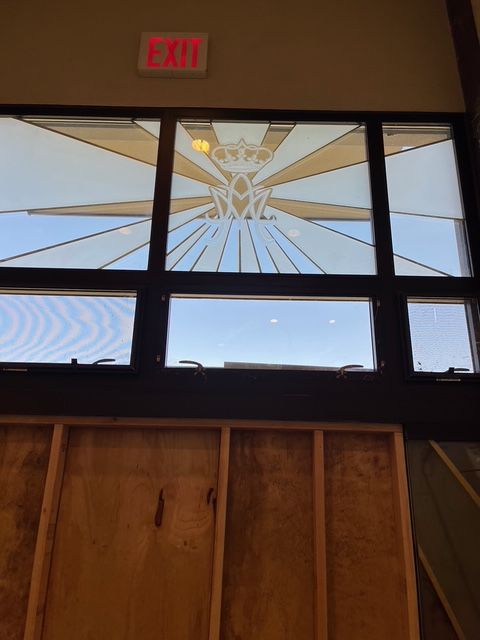 Window with sunburst design and crown over a blue sky; an exit sign is above.