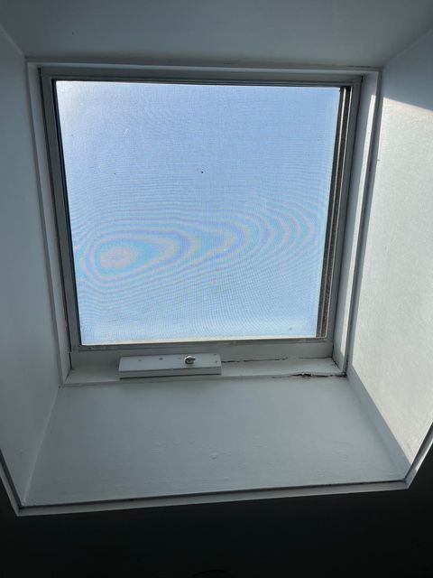 Skylight window with a screen, against a bright blue sky.