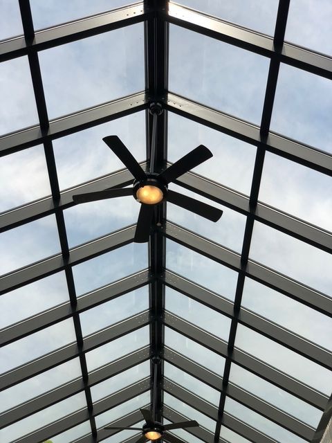 Skylight ceiling with grid pattern and two ceiling fans against a cloudy sky.
