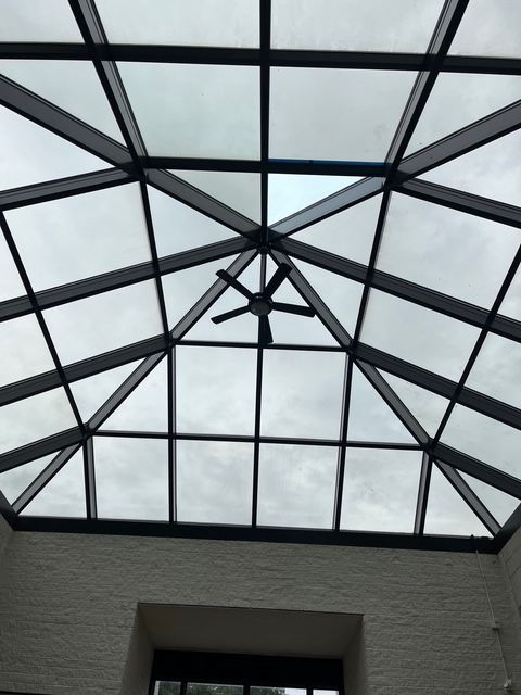 Glass skylight ceiling with black beams and a ceiling fan.