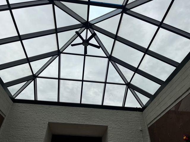 Glass pyramid ceiling with a ceiling fan against a cloudy sky.