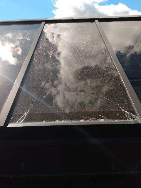 Skylight with cracked glass reflecting clouds and sky; dark frame.