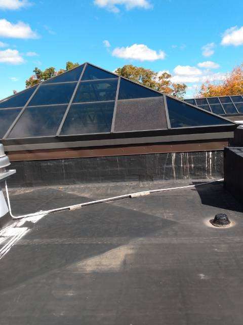 Black flat roof with a pyramid-shaped skylight against a blue sky with clouds.