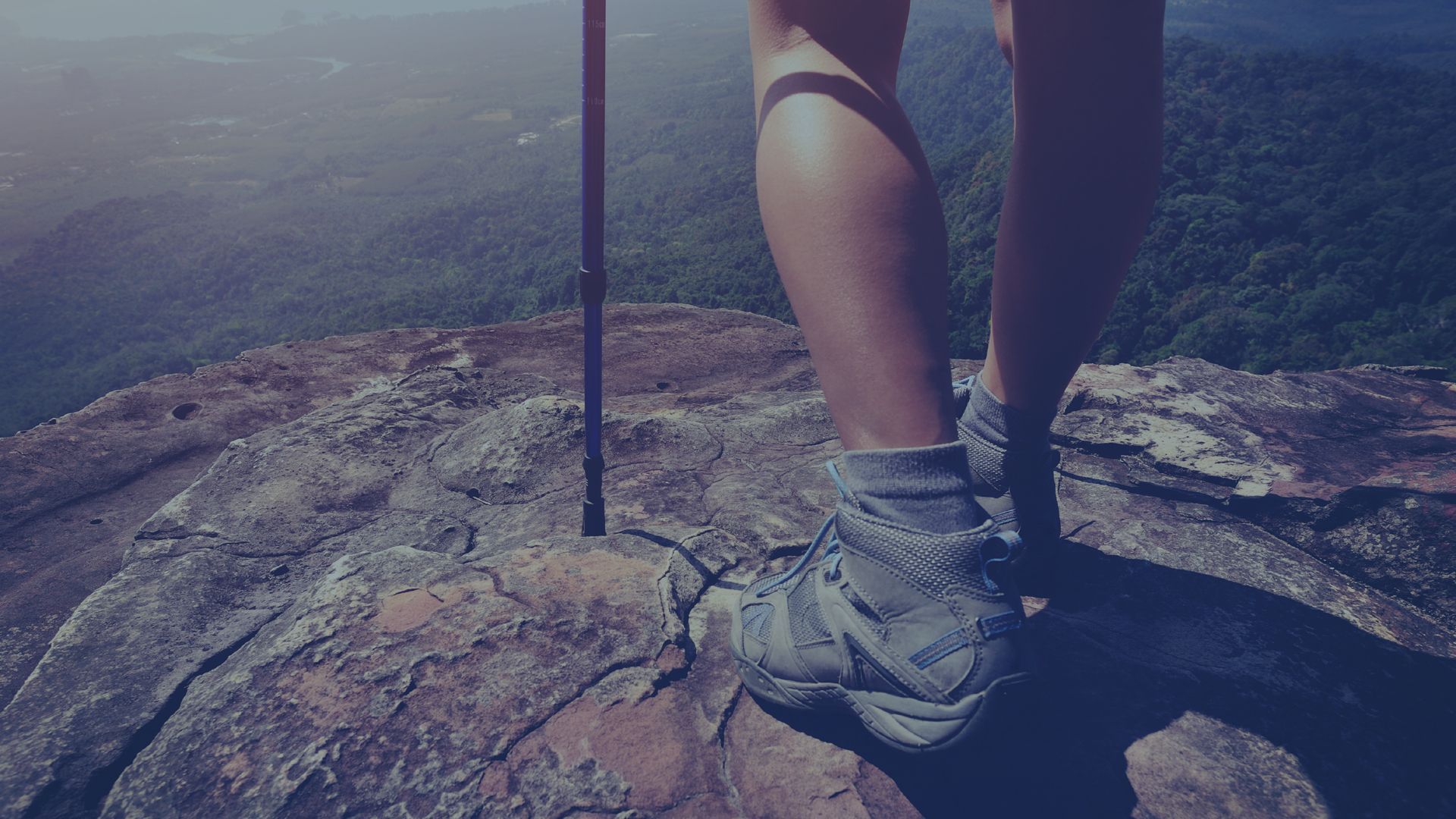 A person is standing on top of a rock holding a hiking pole.