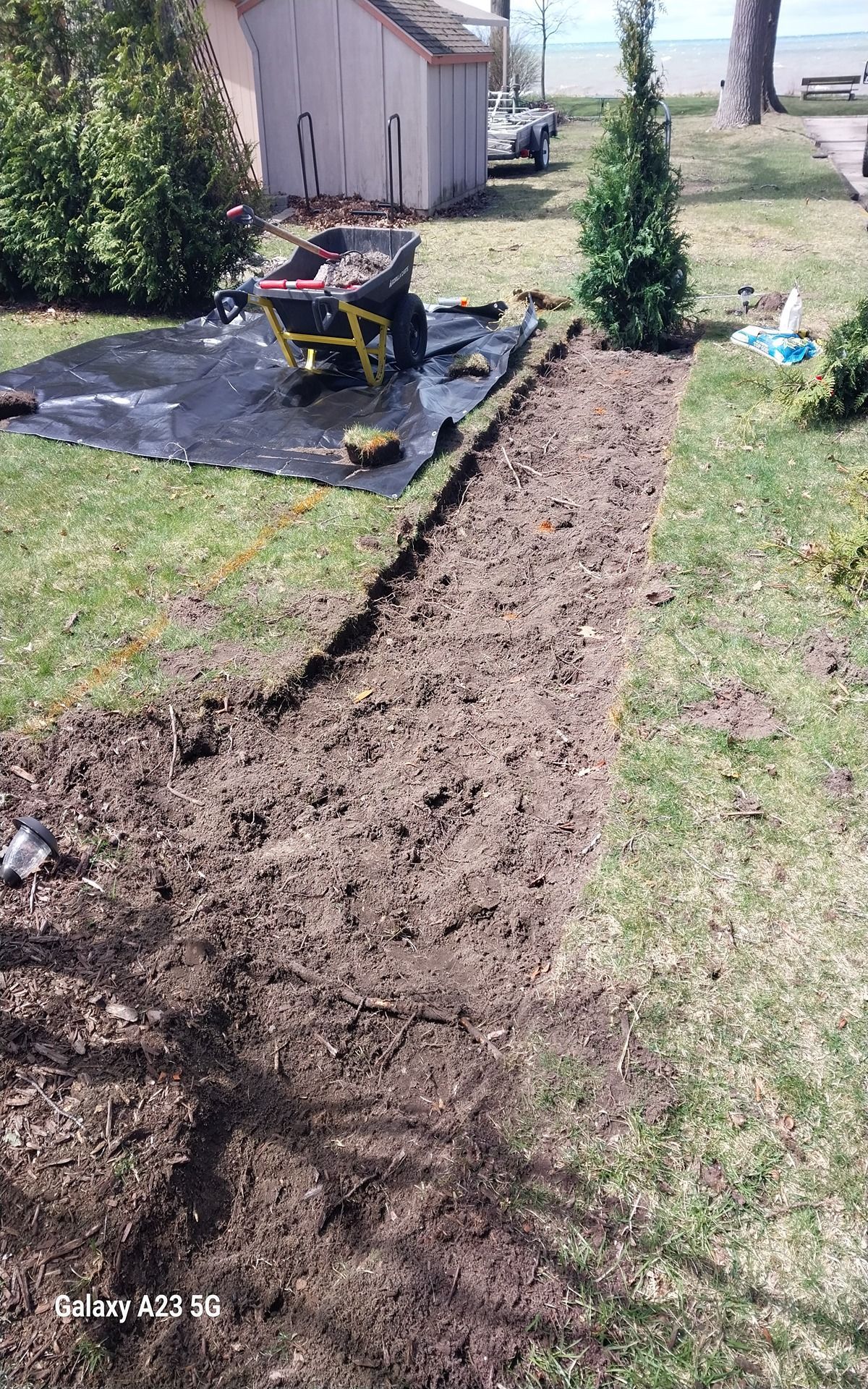 Woman in straw hat smiles, holding wine glass near a lake.