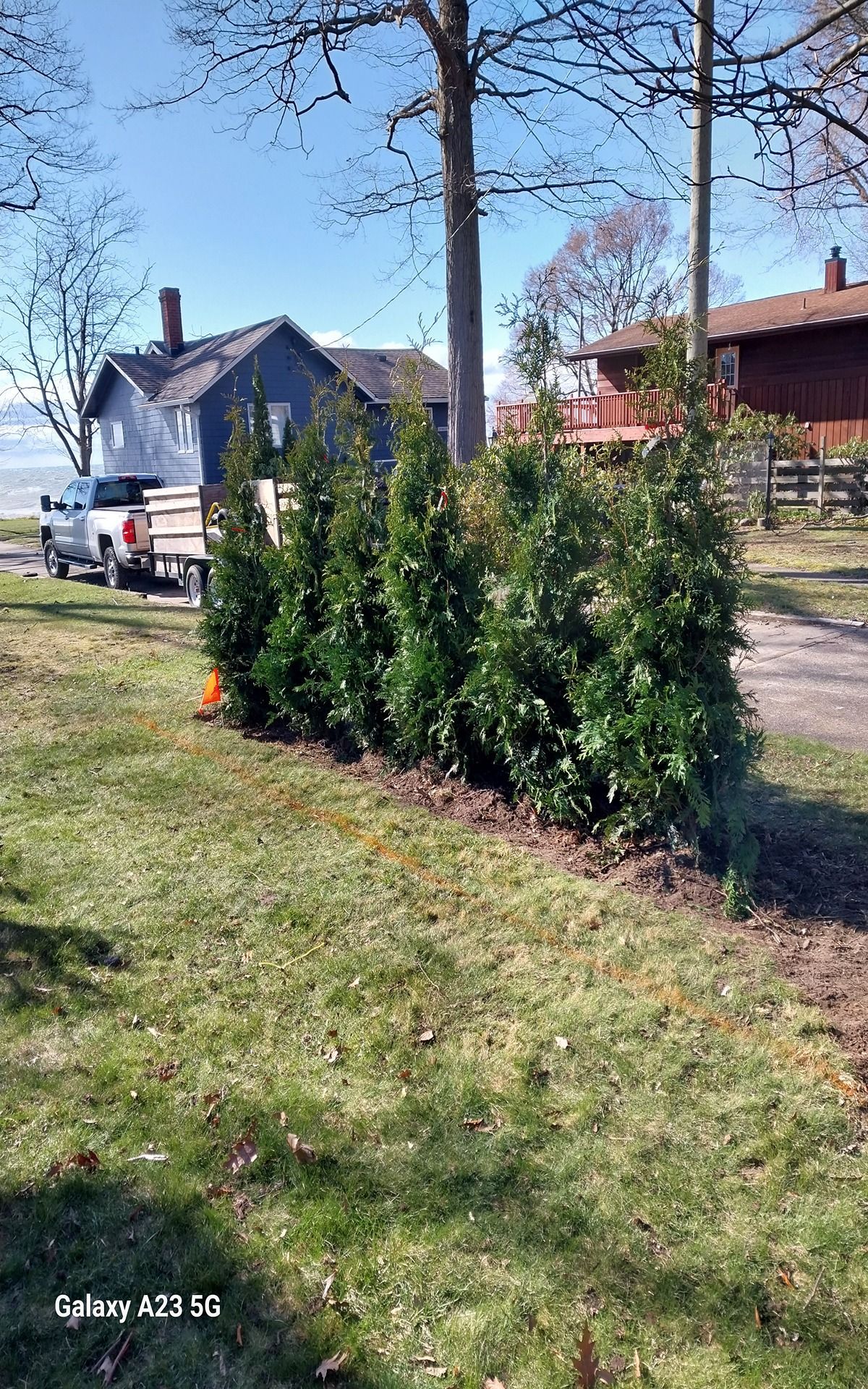 Woman in straw hat smiles, holding wine glass near a lake.