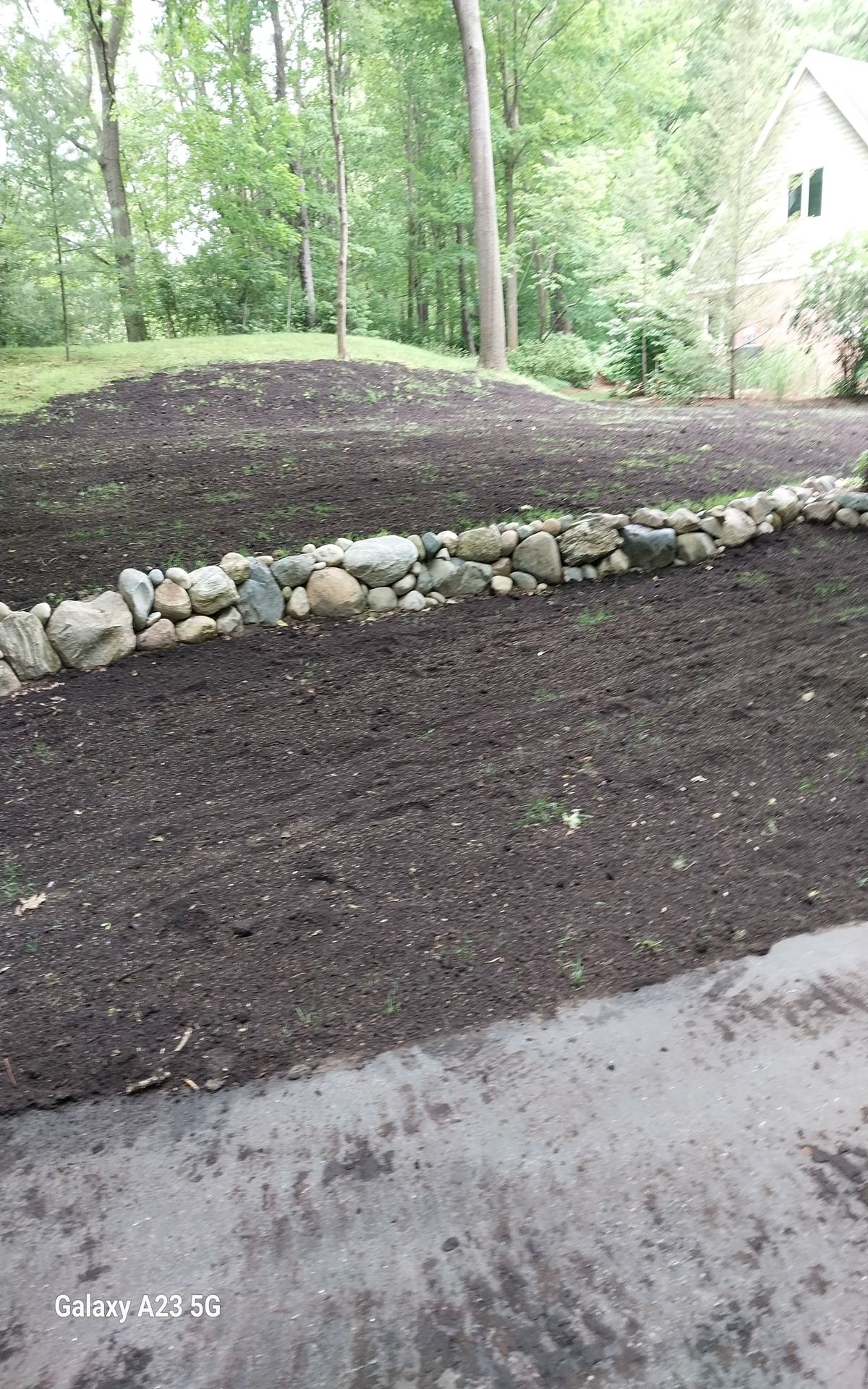 Woman in straw hat smiles, holding wine glass near a lake.