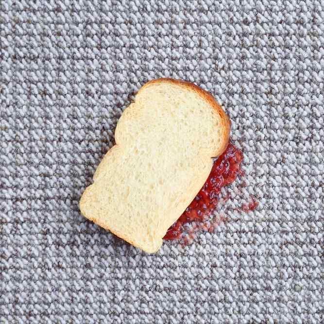 half of a jam sandwich laying face-down on a gray carpet