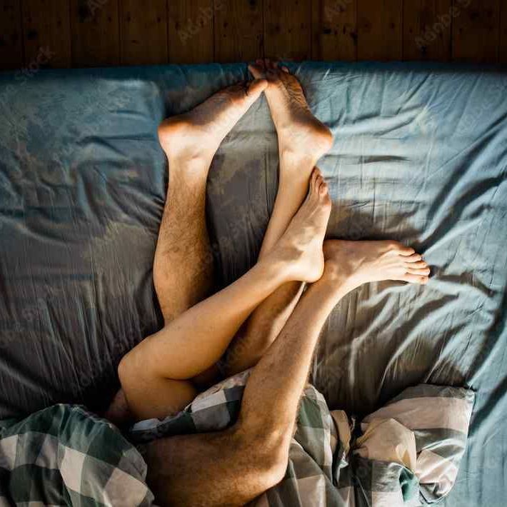 close-up of people's entangled legs and feet at the bottom of their bed