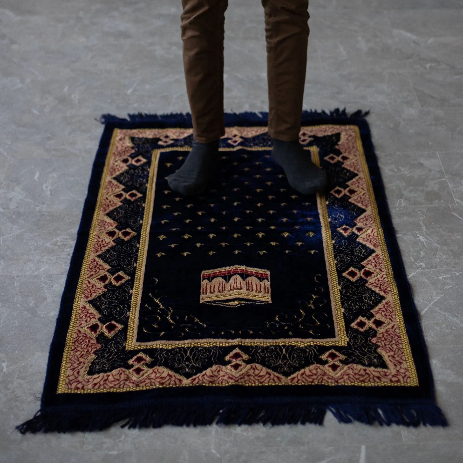 a man stands on an indigo blue and red islamic prayer rug