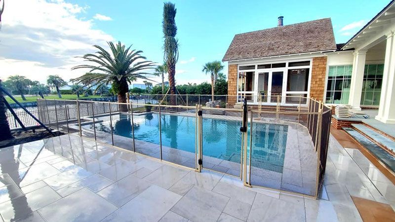 A large swimming pool surrounded by a glass fence in front of a house.