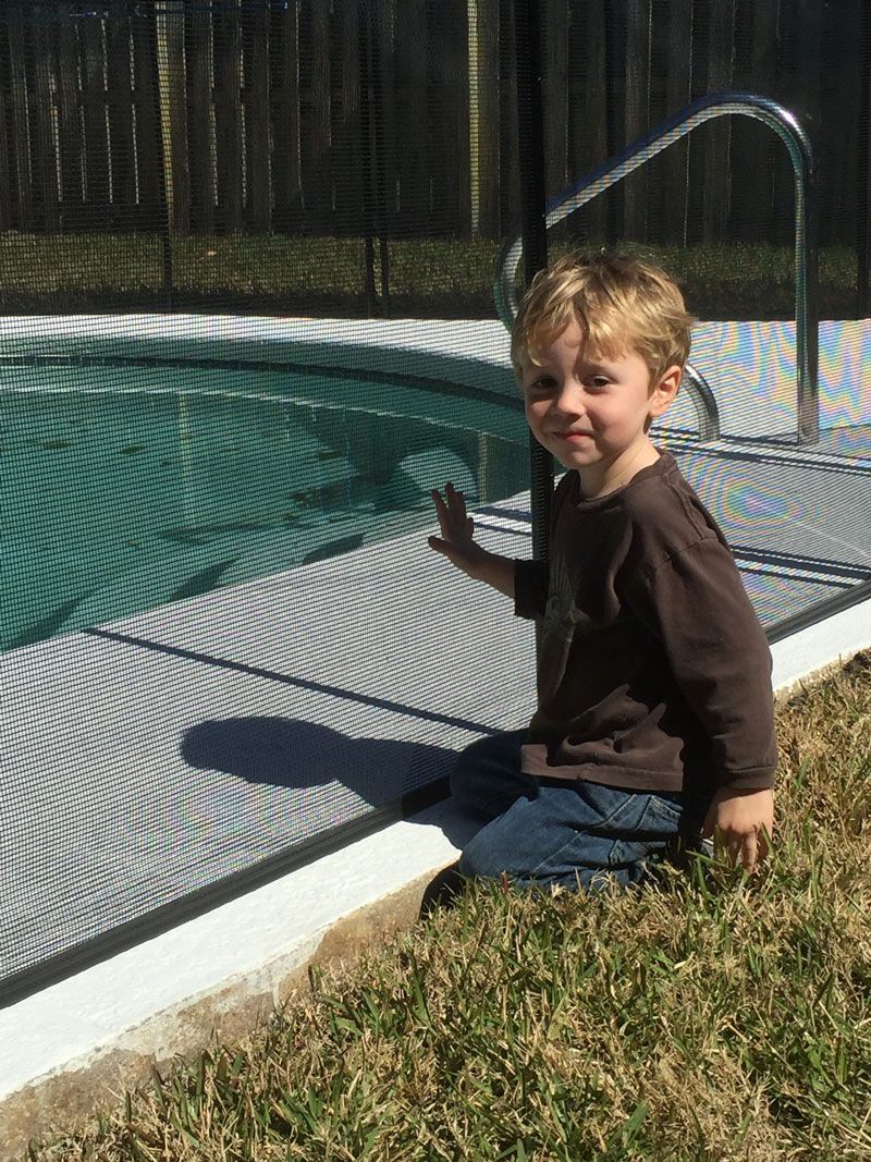 A young boy is sitting in the grass next to a swimming pool.