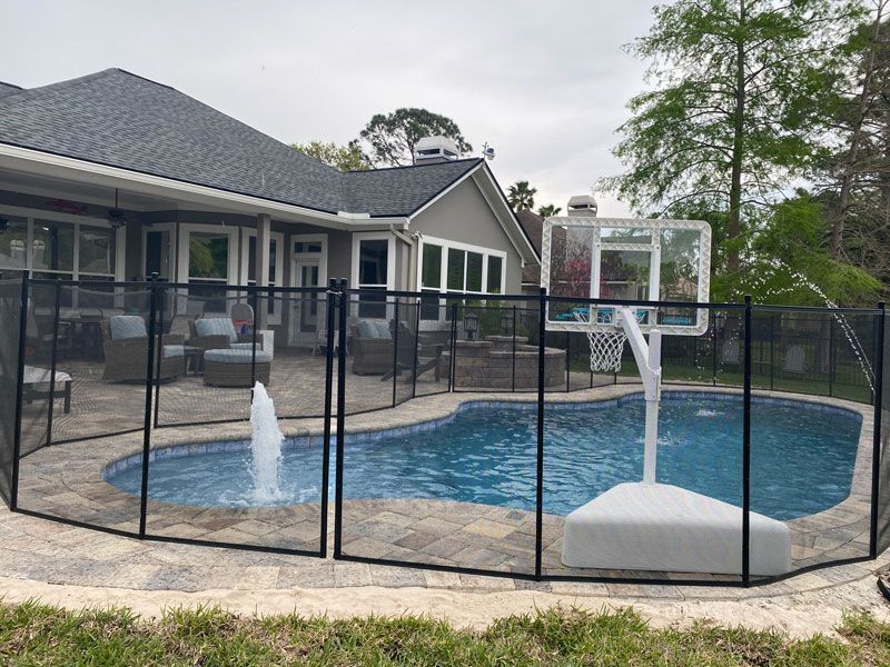A large swimming pool surrounded by a fence and a basketball hoop.