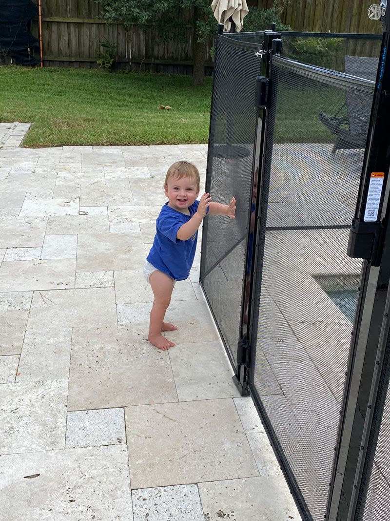 A little boy is standing next to a pool fence.