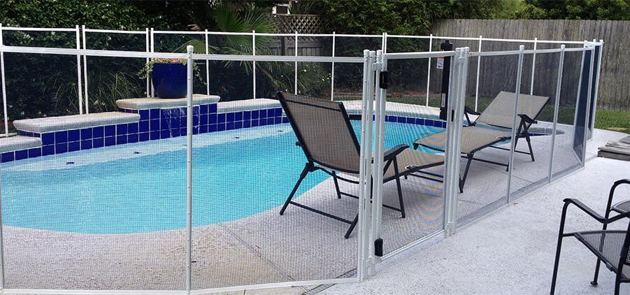 A fence around a swimming pool with chairs and a gate.