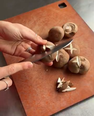 A person uses a knife to cut a cross-shaped decorative pattern into the top of a brown mushroom on a cutting board.